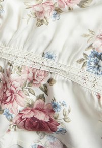 Blomstret stof med rosa og blå blomster på en hvid baggrund, med struktureret blonderkant i midten og rynket detaljering.