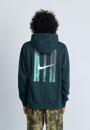 Mörkgrön Nike-hoodie med en stor vit logotyp och grafisk design i ljus teal och mönster på baksidan; mjukt, texturerat tyg.