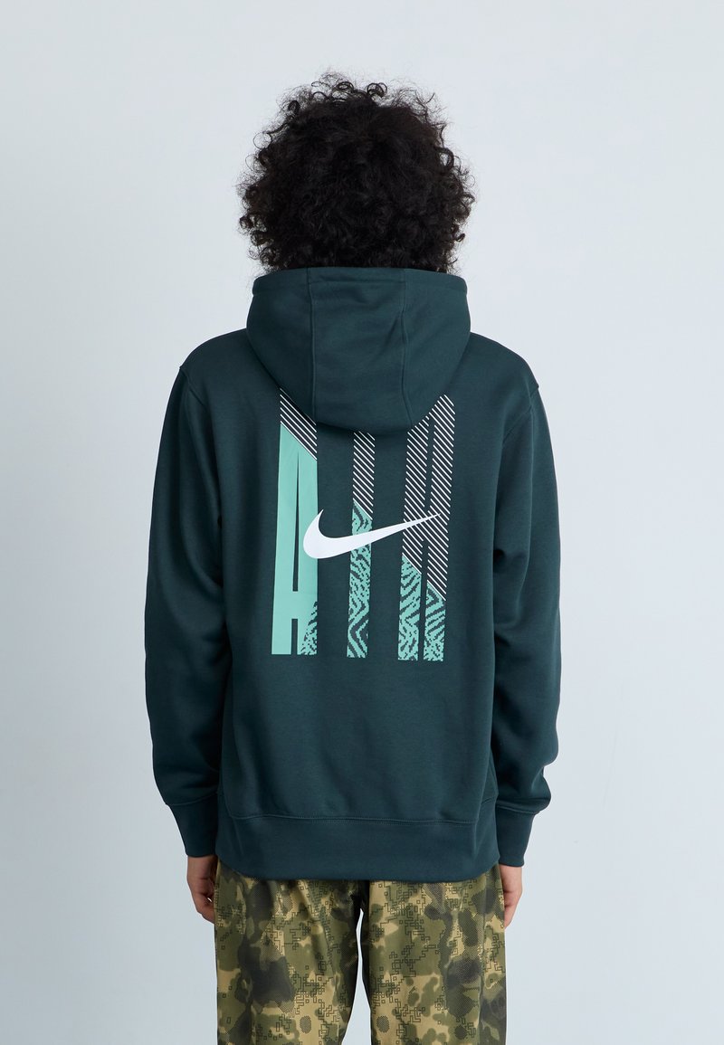 Sweatshirt Nike verde escuro com um grande logotipo branco e design gráfico em azul-turquesa claro e padrões nas costas; tecido macio e texturizado.