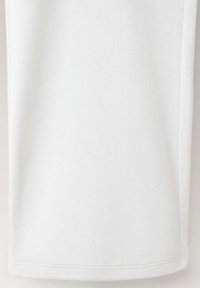 Gros plan sur la partie inférieure d'un vêtement en tissu blanc uni avec des coutures visibles le long de l'ourlet inférieur.