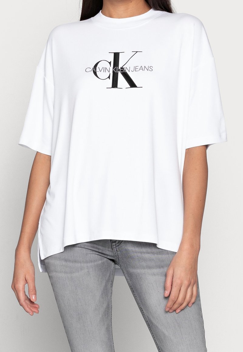 White cotton T-shirt with short sleeves, loose fit, featuring a black "CK" logo and "CALVIN KLEIN JEANS" text in a clean font.