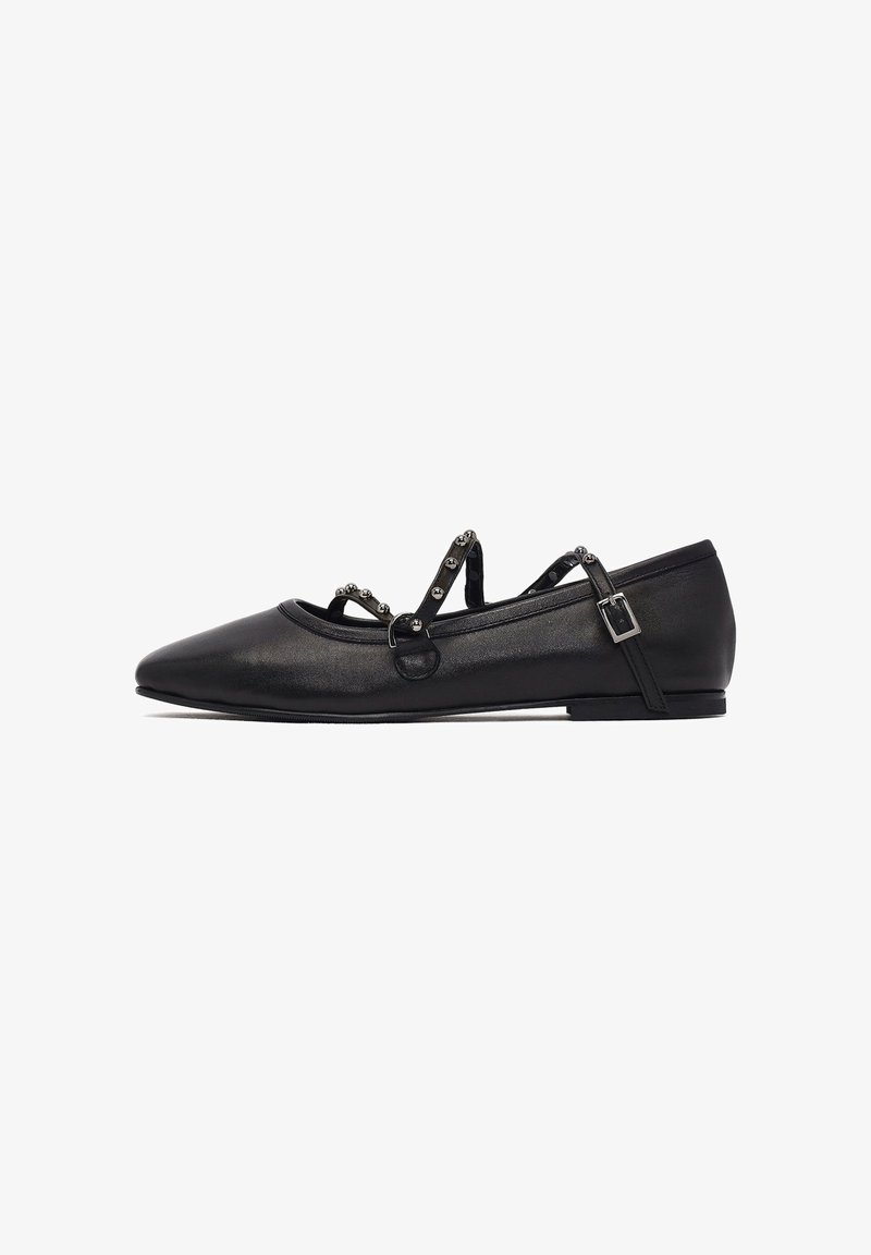 Ballerines noires avec un bout pointu, en cuir lisse, et des brides décoratives à la cheville avec des accents métalliques. Semelle plate.
