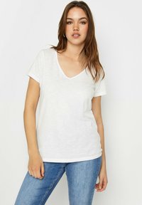 Valkoinen V-kaula-aukkoinen t-paita pehmeässä, kevyessä kankaassa. Lyhyet hihat, rento malli ja hienovarainen heather-kudos. Yhdistetty sinisiin farkkuihin.