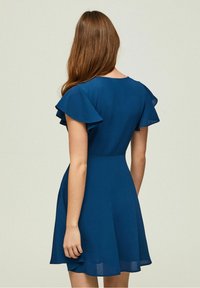 Krátké modré šaty s plandavými rukávy, přiléhavým živůtkem a rozšířenou sukní; vyrobené z hladké, lehké tkaniny s jednobarevným vzorem.