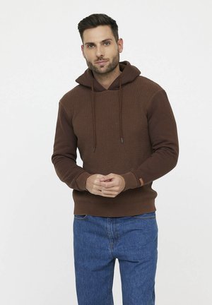 Bruine hoodie met textuur op het lichaam, gladde mouwen, verstelbare trekkoorden en geribbelde boorden, gecombineerd met blauwe denim jeans.