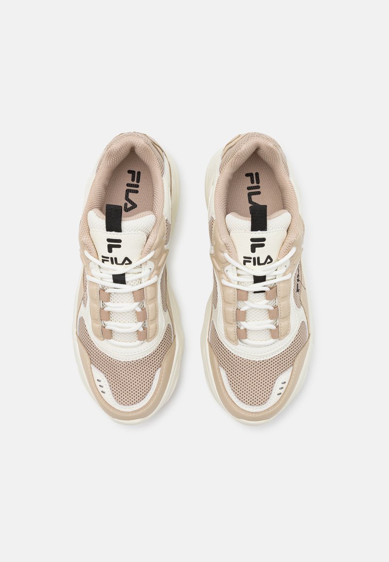 Zapatillas beige y blancas con material de malla y sintético; cuentan con cordones planos, suelas gruesas y un logo negro en la lengüeta.