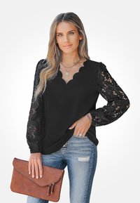 Blouse noire avec un décolleté festonné et des manches longues en dentelle. Associée à un jean bleu déchiré et un sac à main brun.