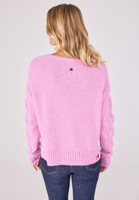 Pastellrosa gestrickter Pullover mit geripptem Saum und Ärmeln. Verfügt über ein Kabelstrickmuster und einen dekorativen schwarzen Knopf auf der Rückseite.