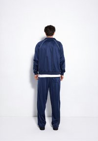 Granatowy dres z kurtką na zamek i luźnymi spodniami. Posiada białe akcenty w szwie i minimalistyczny design. Gładka faktura.