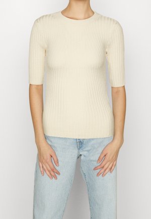 Kremowy prążkowany dzianinowy top z okrągłym dekoltem i krótkimi rękawami, zestawiony z jasnoniebieskimi dżinsami. Charakteryzuje się dopasowanym krojem.