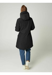 Juoda, su gobtuvu striukė su laisvu siluetu, virš kelių ilgio, turinti lygią tekstūrą ir šonines kišenes, derinama su mėlynais džinsais ir baltais sportbačiais.