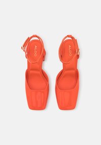 Sandales à talon bloc en cuir verni orange avec une bride de cheville et un design à bout carré, présentant une texture lisse et une semelle intérieure marquée.