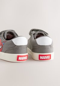 Baskets en toile grise avec un empiècement de talon en cuir blanc et un logo Marvel en caoutchouc rouge au talon, ornées de graphismes Spider-Man sur les côtés.