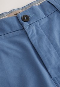 Modre bombažne hlače z gumbno zapiranjem in gladko teksturo. Notranji pas ima kontrastni karo vzorec.