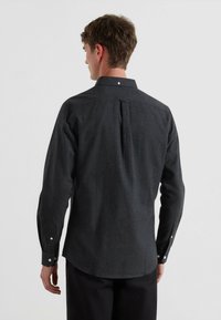 Czarna koszula zapinana na guziki z długimi rękawami, klasycznym kołnierzykiem i plisą z tyłu. Posiada białe guziki na mankietach.