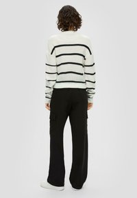 Gestreifter weißer und schwarzer Strickpullover kombiniert mit schwarzen Cargo-Hosen mit Seitentaschen und lockerer Passform, getragen mit weißen Sneakers.