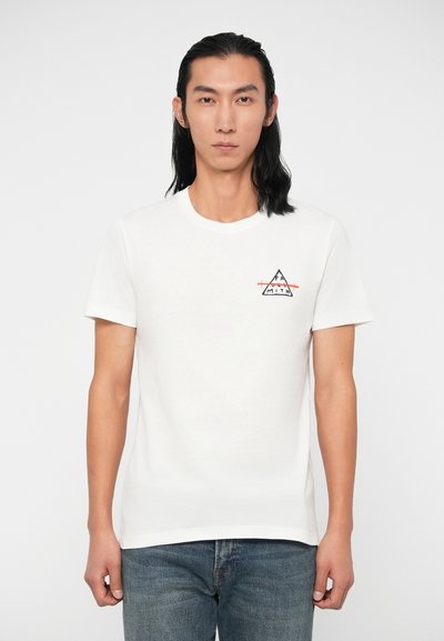 Valkoinen lyhythihainen T-paita, jossa on musta- ja punatrikooinen kolmiomainen grafiikka vasemmassa rinnassa. Pehmeää puuvillamateriaalia ja perinteinen pyöreä kaula-aukko.