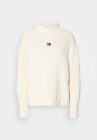 Pull en tricot côtelé blanc avec col montant et petit patch logo Tommy Jeans rouge, blanc et bleu sur la poitrine.