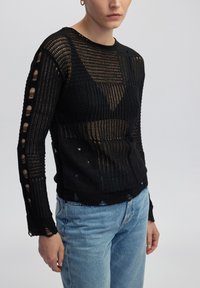 Pull en tricot noir avec un design à motifs, des découpes sur les manches et le corps, un tissu texturé et une coupe décontractée.