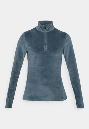 Lys blå fleece-genser med lange ermer, glidelås i halsen og edderkopp-logo som detalj. Glatt tekstur og figurnær design.