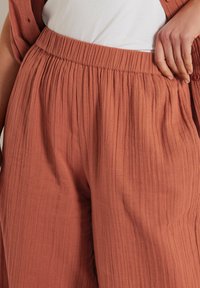 Roodkleurige, gestructureerde wijde broek met een elastische tailleband en verticale plooien voor extra ontwerpelementen. Zacht, ademend materiaal.