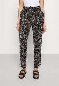 Black patterned trousers featuring a paisley design in red and white, with an elastic waistband and side pockets. Paired with black sandals.
