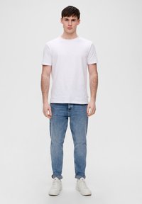 Biała koszulka z okrągłym dekoltem w połączeniu z jasnoniebieskimi d�żinsami i białymi trampkami. Luźny krój z podwiniętymi mankietami na dżinsach, minimalistyczny design.