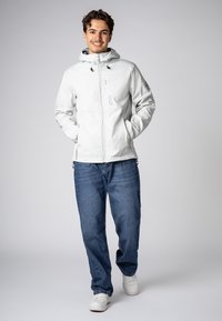 Hellgraue Zip-Jacke mit Kapuze, verstellbaren Kordeln und Logodetails. Kombiniert mit blauen Jeans und weißen Turnschuhen. Glatte Textur.