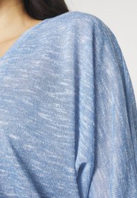 Hellblauer Strickpullover aus einem strukturierten, weichen Stoff; verfügt über einen V-Ausschnitt und lockere, fallende Ärmel. Beinhaltet subtile Farbvariationen.