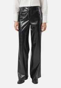Czarne spodnie z szerokimi nogawkami wykonane ze sztucznej skóry o błyszczącym wykończeniu, z szlufkami, przednimi kieszeniami i wysokim stanem, w zestawieniu z czarnymi butami.