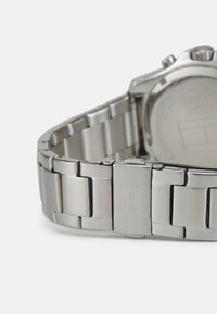 Bracelet de montre en acier inoxydable argenté avec finition brossée, maillons et fermoir avec un logo gravé. Texture lisse avec un éclat subtil.