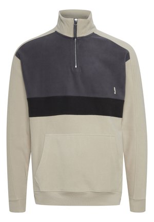 Fleece pullover in beige and dark gray with a half-zip collar, front pocket, and black accent band across the chest. Soft texture.