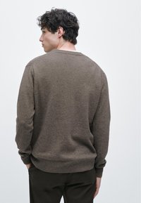 Brązowy dziergany sweter z okrągłym dekoltem, prążkowanymi mankietami i krawędzią, dopasowany fason, widziany od tyłu na jednolitym białym tle.