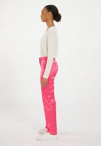 Pantalons roses brillants avec une coupe ajustée, associés à un haut clair à manches longues ample et des baskets blanches. La vue de côté montre la silhouette.