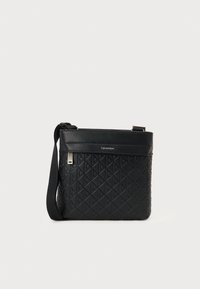 Svart crossover-veske med et teksturert skinneksler som har diamantmønster, justerbar stropp og sølvfarget hardware-detaljer.