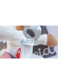 Giocattolo morbido in peluche con corpo bianco, dettagli marroni, anello grigio rotondo e etichetta rossa. I dettagli dell'etichetta includono i marchi CE e UKCA.