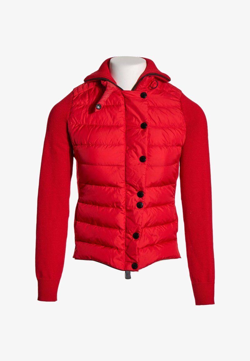 Veste rouge avec devant matelassé, boutons noirs, manches longues tricotées et col montant avec fermeture éclair et cordon.