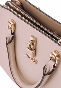 Borsa beige realizzata in materiale sintetico, con hardware dorato, chiusura con zip e doppi manici con dettagli in contrasto.