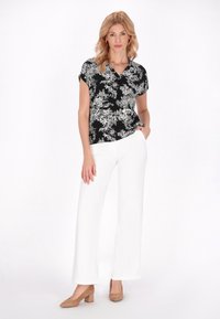 Blusa a fiori in bianco e nero con maniche corte, abbinata a pantaloni bianchi a gamba larga e scarpe con tacco a blocco beige.