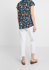 Camisa de estampado floral de manga corta en color marino, con flores amarillas y blancas. Combinada con pantalones recortados blancos y sandalias de cuña marrones.