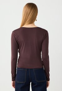 Bruine lange mouwen top met een ronde halslijn, voorzien van subtiele ruches aan de zijkanten en een gladde, elastische stof; gecombineerd met donkerblauwe jeans.