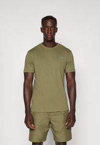 Ελιά πράσινη βαμβακερή μπλούζα κοντομάνικη, με στρογγυλή λαιμόκοψη, στενή εφαρμογή και μικρό λογότυπο Lacoste στο αριστερό στήθος.