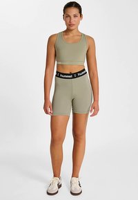 Zestaw sportowy składający się z jasnego oliwkowego krótkiego topu i dopasowanych, wysokich szortów, wykonanych z elastycznego materiału z czarnym paskiem w talii z logo.