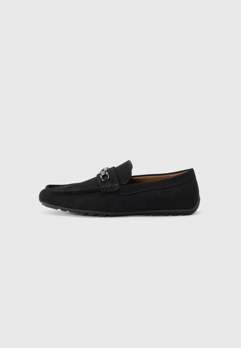 Mocasines de ante negro con punta redondeada, correa decorativa y detalle en metal en tono plata. Suela de goma flexible para tracción y comodidad.