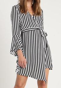 Gestreiftes Wickelkleid in Schwarz und Weiß. Hat weit ausgestellte Ärmel, einen Knoten in der Taille und einen asymmetrischen Saum. Leichter Stoff.