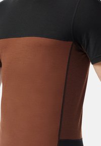 Camiseta deportiva de manga corta con una parte superior negra y una sección inferior marrón texturizada con un acabado suave y costuras en contraste.