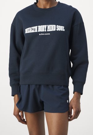 Person wearing a navy sweatshirt with "HEALTH BODY MIND SOUL" and shorts, cropped at mid-thigh, standing against a plain background.