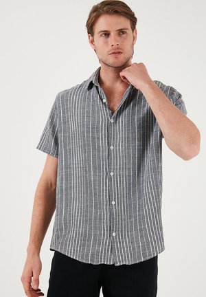 Camisa de manga corta, tipo polo, con un patrón de rayas en blanco y negro, hecha de una tela ligera con una textura suave y un corte holgado.