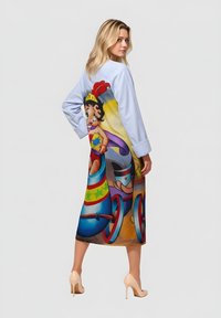 Vestido azul con un estampado de dibujos animados que muestra a un personaje en un vehículo colorido. Mangas largas, largo hasta la rodilla, tela que parece suave y ligera.