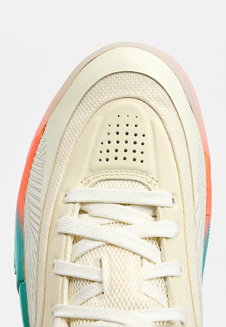 Zapatilla con parte superior de crema clara, paneles de malla texturizados y suela translúcida colorida con acentos en naranja y verde azulado. Diseño con cordones visible.